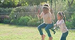 Two children playing on a swing in their backyard on a sunny day. Adorable sibling sisters bonding and having fun together at park in summer. Happy, playful and active girls enjoying their childhood