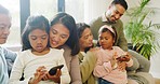 Happy diverse family using phones to browse online and watch videos while relaxing on the couch together. Little girls searching the internet while bonding with their parents and grandparents