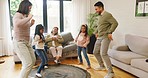 Cute children showing their parents dance moves in the living room with grandparents laughing and watching on the sofa. Family having fun and being silly together on holiday inside on a sunny day