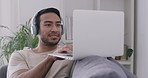 Music dj streaming on laptop, wearing listening headphones and making new songs on online musical subscription software. Smiling, happy and relaxed man sitting on home sofa and browsing on technology