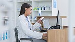 Young pharmacist working on computer at a pharmacy counter. Woman using technology to access drug database, does inventory checkup and dispensing online medicine prescriptions in a drugstore