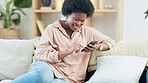 Young woman smiling and laughing while texting on a phone at home. Cheerful female chatting to her friends on social media, browsing online and watching funny internet memes while relaxing on a couch