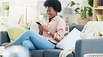 Young African American woman on phone, relaxing, sitting on couch and laughing. Female is alone and texting, using internet or playing a game. She is showing joy and smiling
