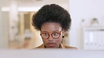 Busy teacher working on a computer inside and looking focused. Face of young education worker with afro and glasses typing assignment or grading test papers online at a desk inside a modern campus. 