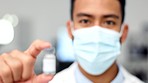 Hand of doctor holding a vaccine for a virus or covid inside against a blurred background. Closeup portrait of a medical researcher wearing a mask and showing a glass vile with flu injection at a lab