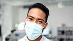Happy male scientist wearing a mask and protective glasses in a laboratory. Portrait of a young healthcare specialist looking confident in finding a cure. Cheerful doctor standing in the research lab