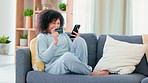 Woman excited to make purchase on mobile. Young lady is relaxing on couch indoors holding credit card, smiling, laughing and dancing after buying something on the internet with her phone