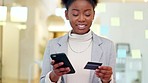 Woman using a phone and bank card to make an online payment, standing in an office. Young african business woman typing credit details into a banking app for virtual shopping or wireless purchase