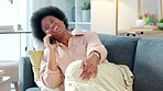 Comfortable at home on a couch talking on the phone with a best friend. A young African woman relaxing on a sofa chatting and laughing on a call on a weekend. A relaxed female enjoying gossip