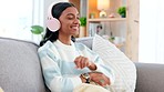 Woman wearing headphones and using a phone to listen to her a playlist while relaxing on a sofa at home. Carefree female dancing and having fun alone on a couch, enjoying her free time on a weekend