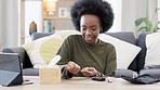 Happy African American woman using a glucose monitoring device at home. Smiling black female checking her sugar level with a rapid test result kit, daily routine of diabetic care in a living room