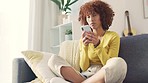 Frustrated woman texting on phone while sitting on a sofa at home. Young female feeling annoyed with a negative response or email. Bored lady having an online argument on social media or a breakup