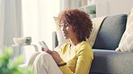 Relaxed black woman texting on a phone while sitting on the living room floor at home. Young African American female browsing social media while enjoying free time chatting to friends on the weekend