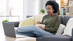 Happy african american woman streaming online movies on a laptop while snacking on popcorn and relaxing on a sofa at home. Black female enjoying a comedy, eating, laughing and having fun on a weekend