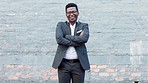 African American businessman in suit and glasses standing, smiling and crossing his arms against grey wall background. Young entrepreneur is pleased at his business succeeding. Hard work paying off