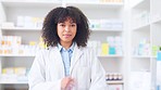 Happy and confident pharmacist standing in front of medicine shelves in a drugstore. Young female healthcare professional standing with her arms crossed, wearing a lab coat and smiling in a pharmacy