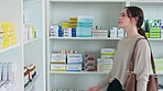 Patient grabbing pills from shelf at medical retail drug store to take care of her health and wellbeing. Young lady finds the right medicine on the shelves to treat her flu sickness at chemist shop