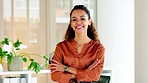 Confident stylish woman laughing with arms crossed and standing inside a modern office near a window. Face portrait of a happy hispanic female entrepreneur looking cheerful about successful business