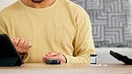 A young man with diabetes testing his blood sugar levels at home. A diabetic male student using a glucometer inside his house. Closeup of a guy with a chronic disease monitoring his healthcare