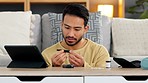 Man suffering from diabetes checking his sugar levels with a home test kit and digital tablet in the living room. One Asian male with a chronic illness or disease pricking himself for a blood test