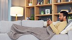 Asian man yawning while watching and streaming movies and series online on a phone while relaxing on the couch alone at home. Tired young male feeling sleepy while playing live games on the internet