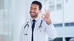 Portrait of male doctor doing an ok sign with fingers. Young healthcare worker or medical professional showing okay hand gesture after giving a successful treatment in a modern hospital clinic