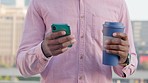 Trendy designer texting on a phone while drinking coffee in a reusable cup in the city. Hands of a guy taking a break to browse apps, scroll social media and search the web from an office balcony
