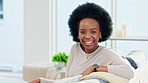 Portrait of a happy afro woman relaxing at home on the weekend. Beautiful casual African American female smiling and enjoying a relaxed Sunday afternoon in her bright living room with copy space