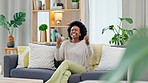 African woman celebrating a new job while sitting at home on a couch. A young female's loan is approved via an email on her phone. A happy and excited lady cheering for a promotion on a sofa