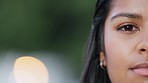 Half face portrait of a woman looking thoughtful with copy space. Closeup of a cute indian girl isolated on blurred background with bokeh. Head of a young female with dark skin, staring and blinking