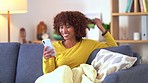Woman texting and scrolling on social media online on a phone while relaxing on the couch at home. One young black woman browsing on social media and searching the internet while sitting on the sofa