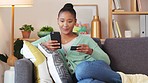 Woman making an online payment with a phone and credit card alone at home. Happy and comfy black female smiling while buying and shopping for items on the internet. One relaxed girl banking on an app