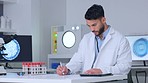 Male scientist writing notes while doing medical research in a  laboratory. Happy researcher writing experiments details and test results on paper while sitting with sample tubes and a digital tablet