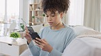 Young woman shopping online using a credit card and phone while looking happy and excited at home. Female with a curly afro finding a sale and making a purchase while sitting in the living room
