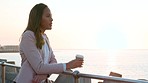 Business woman taking a break in the city at sunset, drinking coffee and enjoying the relaxing view of the ocean. Young female daydreaming against a background of the sun, traveling for work