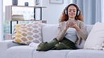 Happy woman enjoying her favorite song or singer on a phone, using headphones. African American female listening to karaoke music while sitting on a sofa. Smiling lady dancing to a beat or rhythm. 
