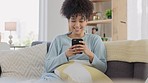 Happy black woman texting on a phone while relaxing on a sofa at a home. Young African American browsing social media, enjoying the weekend and chatting to her friends while laughing at funny memes 