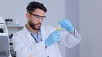 Serious male scientist analyzing liquid in a beaker in a laboratory. Professional biochemist testing yellow fluid, conducting an experiment to find a cure for a virus in a medical research facility