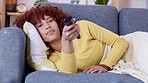 Woman watching tv and changing channels while relaxing on a sofa at home. Carefree and relaxed young female enjoying a weekend of fun entertainment by streaming movies, series and shows on television