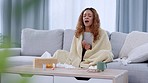 Sick woman sneezing on lockdown on the couch at home wrapped in blanket with medicine and tissues. Young female feeling ill and suffering from covid, a flu virus or a cold infection during quarantine