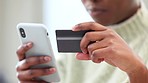 Woman holding credit card, shopping online with her phone and using banking app for secure payment for her internet order. Closeup of happy black female shopper at home buying and paying bills on web