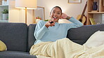 Relaxed, carefree and happy young woman, laughing while enjoying a funny movie or comedy series at home. Switching TV channels, finding something to watch and turning up the volume over the weekend