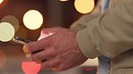 Closeup hands typing a message on a phone. Fingers sending sms or chatting on social media. Man using mobile device to communicate with friends on app while standing against a bokeh lights background