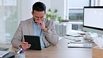 Sick business man suffering from a cold, flu or covid. Office executive sneezing, feeling ill with hay fever. Male entrepreneur blowing his nose in a tissue or wipe at a desk holding a digital tab.