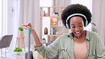 Excited, happy young woman dancing and singing while wearing headphones in her living room and cleaning a home. A casual female doing a silly and funny dance while having fun doing domestic chores