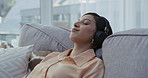 Wearing headphones, listening to relaxing music from phone and enjoying a calm, zen and peaceful day at home. Happy and relaxed woman sitting on a living room sofa and meditating with binaural songs