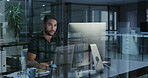 Businessman working late on a computer in an office at night. Young entrepreneur reading emails, research online and compiling reports while planning ideas for deadlines looking satisfied