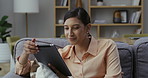 Woman on tablet, sitting and reading ebook while thinking on her couch. Casual female relaxing on her sofa looking through social media feeds. Person holding touchscreen searching the web