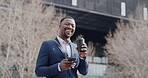 Ambitious, motivated and smiling businessman texting on phone, drinking takeaway coffee and dreaming of success in city. Happy and confident executive standing during morning routine commute to work