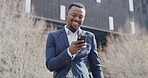 Trendy businessman texting on phone smiling, looking happy, successful after receiving good news while outside in urban city. A stylish corporate professional with a cellphone checking email message